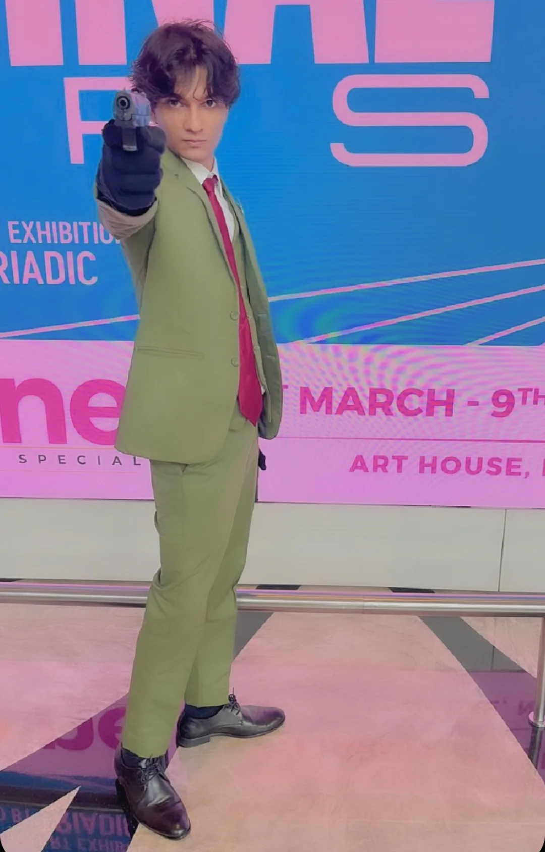 Green-suit cosplay posing with a prop against a convention display