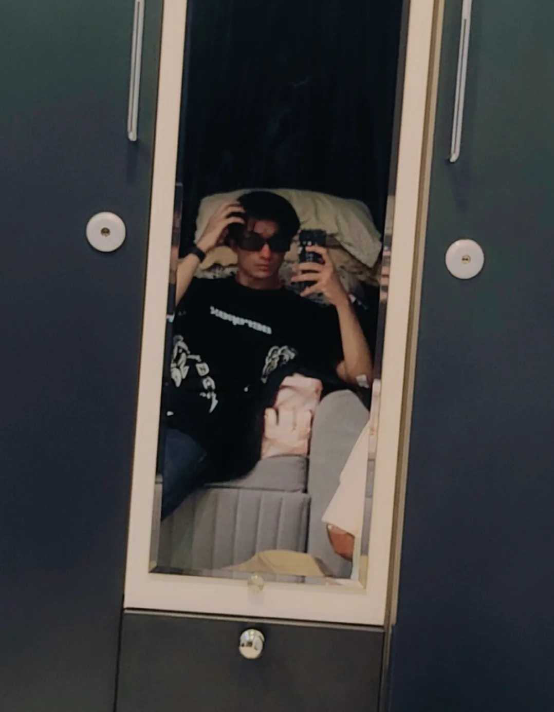 Seated mirror portrait in a black shirt and sunglasses